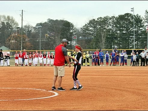 A coach addresses players gathered on the field at opening ceremonies