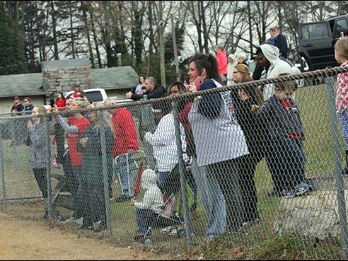Families watching opening day from behind the outfield fence at Doyle Street Park
